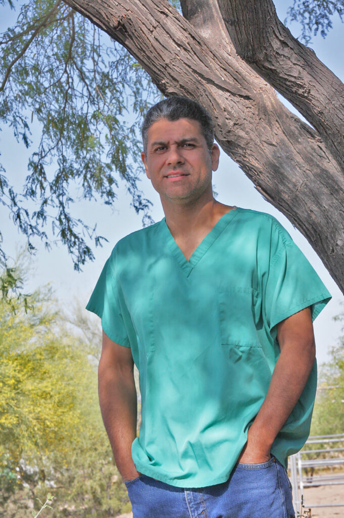 Man in scrubs standing by tree.