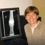 Here's an alt tag for the image: Smiling woman with knee X-ray on monitor.